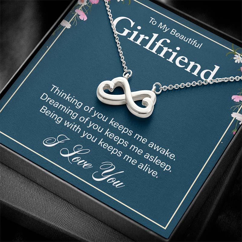 Angled view of a silver infinity heart necklace displayed inside a classic black gift box with a girlfriend message card