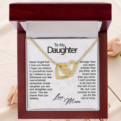 A gold necklace with two interlocking heart-shaped pendants resting inside an open, dark mahogany wood gift box with built-in LED illumination. The necklace is displayed over a white card addressed "To My Daughter" featuring a sentimental message, signed "Love, Mom" in cursive script.