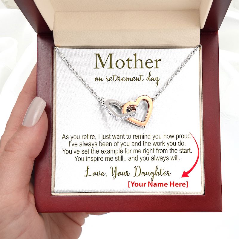 Necklace with interlocking heart pendants and a personalized message for mom retirement in a gift box hold by a hand.