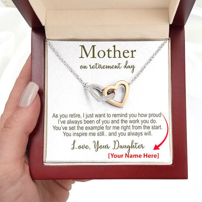 Necklace with interlocking heart pendants and a personalized message for mom retirement in a gift box hold by a hand.