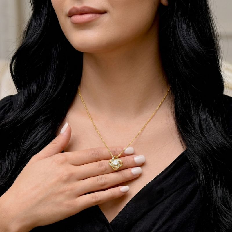 Gold Knot Necklace: a woman wearing a gold knot necklace with a pendant, touching her chest.