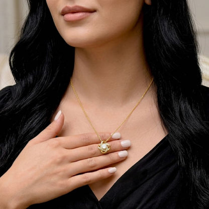 Gold Knot Necklace: a woman wearing a gold knot necklace with a pendant, touching her chest.
