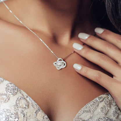 Close-up of a woman wearing a silver necklace with a heart-shaped pendant, hand touching her neck.