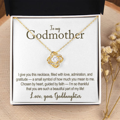 Gold necklace with heart-shaped pendant in a gift box with message addressed to a godmother, on a wooden surface.
