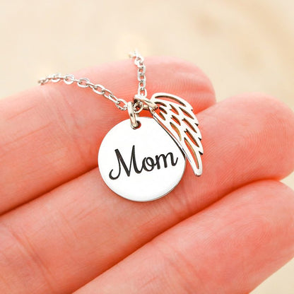 Silver necklace with 'Mom' pendant and angel wing on a hand against a beige background