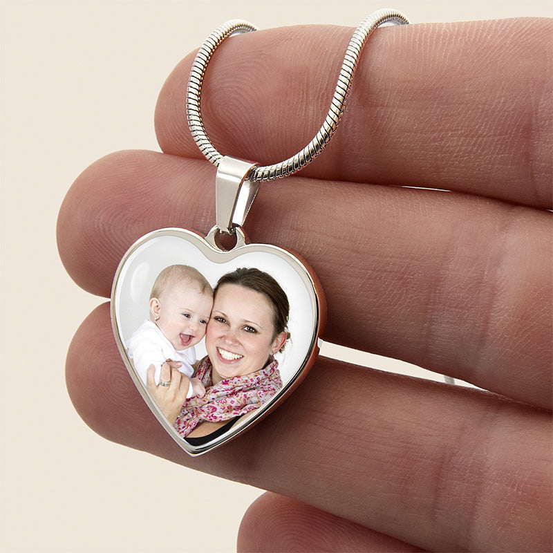 photo necklace: heart-shaped pendant with a photo of a woman and a baby held between fingers on a beige background