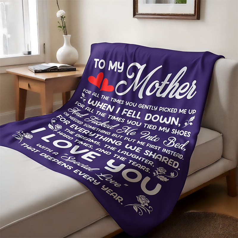 Purple blanket with a sentimental message for mom in white text, laid on a couch, in a cozy living room.