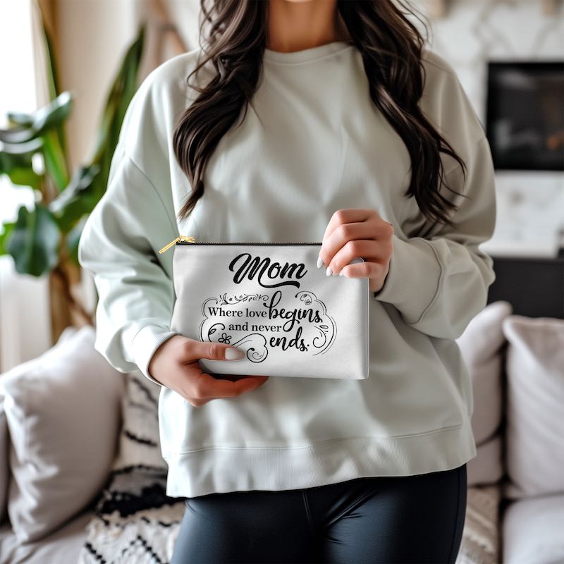 Woman holding a cosmetic bag with 'Mom Where love begins and never ends' text against a living room background