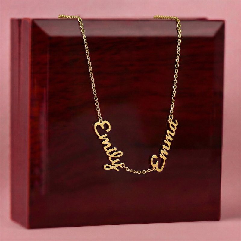 Gold necklace with 'Emily' and 'Emma' on a red box with pink background
