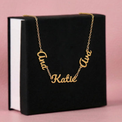 Gold name necklace with 'Ana''Katie'and 'Ava' cursive name pendants on a black box with pink background