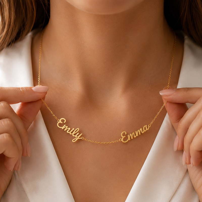 Gold name necklace with 'Emily' and 'Emma' on a person wearing a white top.