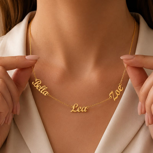 Gold name necklace with 'Bella', 'Lea', and 'Zoe' on a person wearing a white outfit.