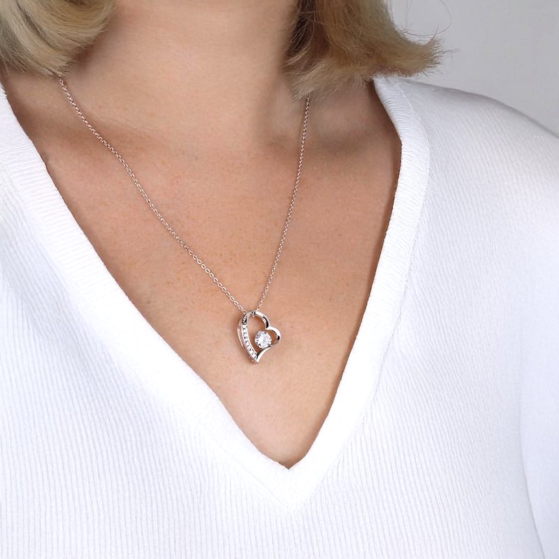 Silver necklace with a heart-shaped pendant padded with cubic zirconia stones and one big round cut Zirconia, worn by a woman in a white shirt.