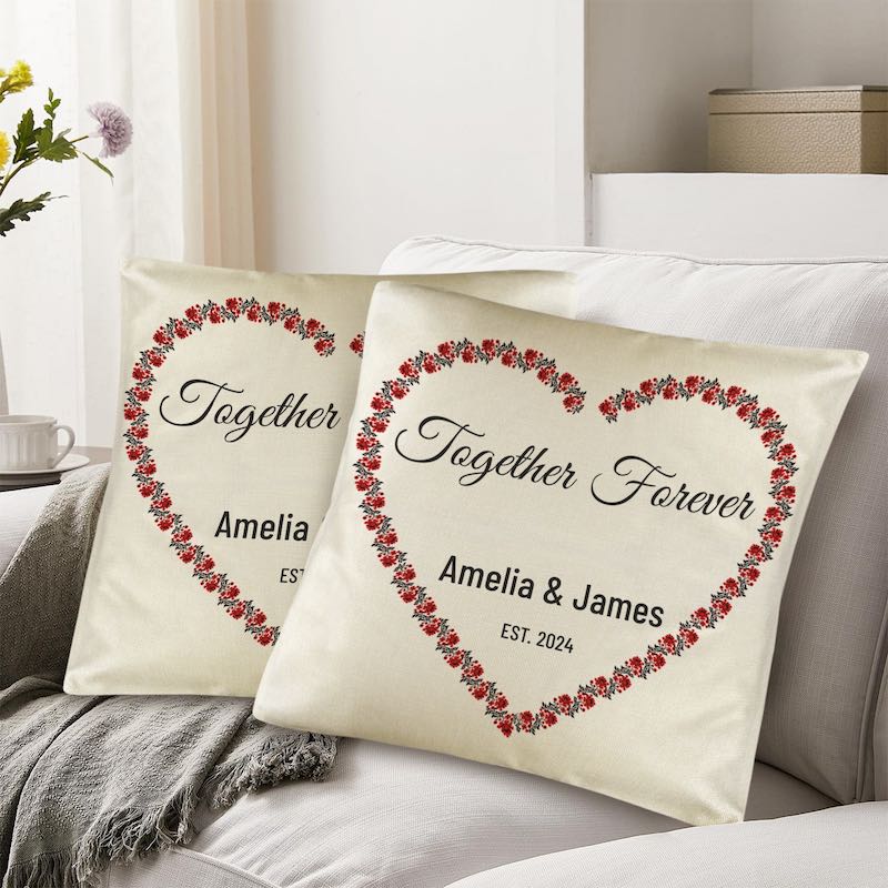 Two decorative pillows with floral heart designs and personalized text on a couch.