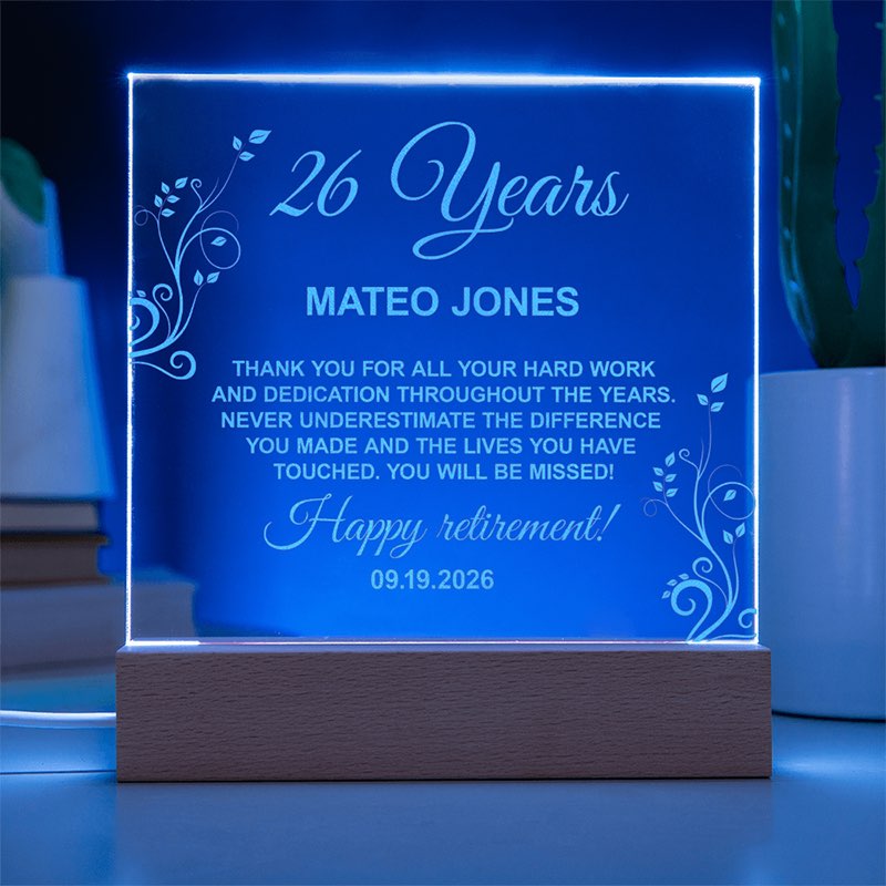 Illuminated personalized acrylic retirement plaque glowing blue on a wooden LED base, featuring floral engravings and a message honoring Mateo Jones for 26 years.
