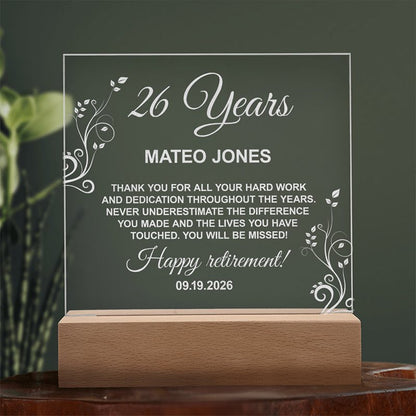 Personalized clear acrylic retirement plaque on a wooden base with printed floral details and text, set against a dark backdrop with a potted plant. - Gifts For Family Online