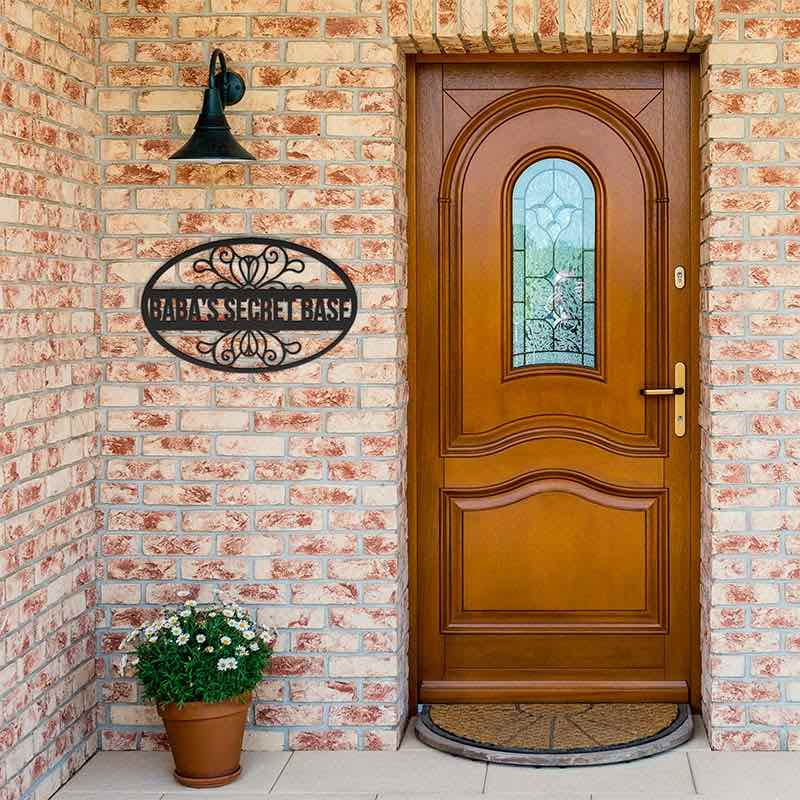 Black metal sign displayed on a brick wall, next to a wooden front door with decorative glass panel.