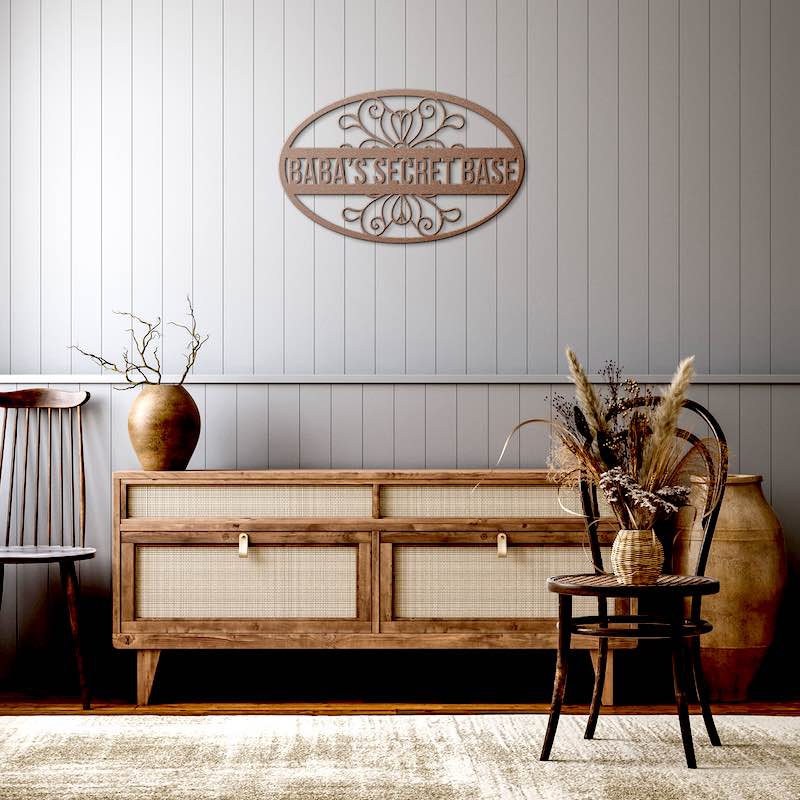 Wooden sideboard with decorative items against a gray paneled wall with 'Baba's Secret Base' cooper sign.