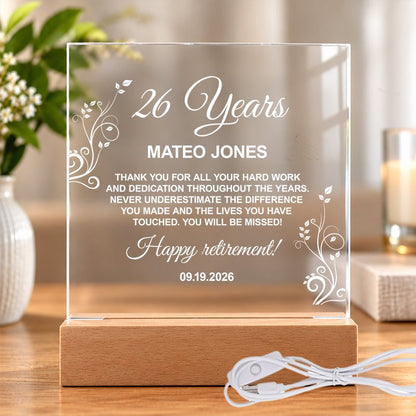 Personalized clear acrylic retirement award plaque on a wooden stand, engraved with "26 Years," "Mateo Jones," and a thank-you message with floral details.