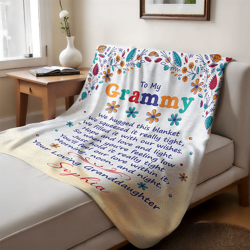 Blanket with a floral design and a sentimental text from granddaughter to grandma, laid on a couch in a living room.