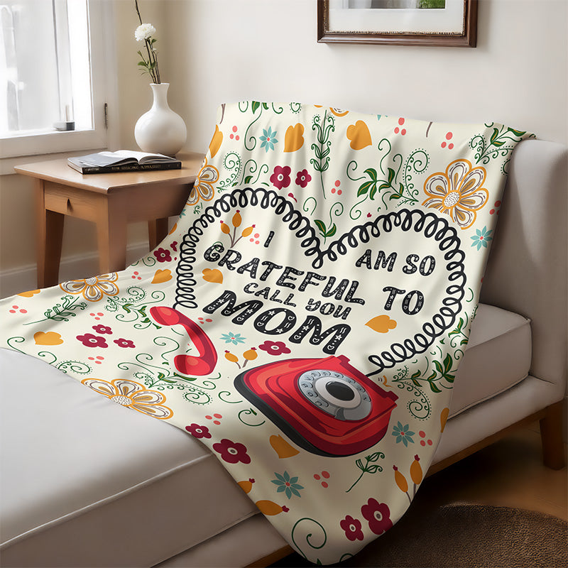 Decorative blanket featuring a floral and phone design with the text “I am so grateful to call you Mom,” displayed on a couch in a living room.