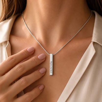 Silver necklace with a bar pendant worn by a person, close-up of the necklace and hand.
