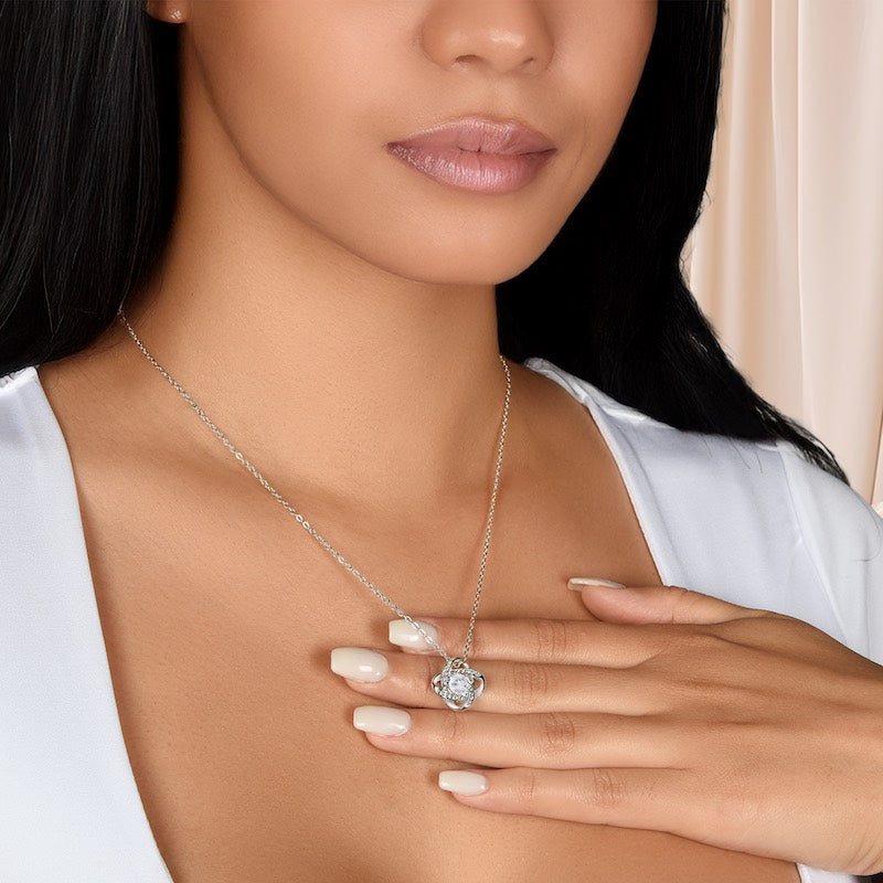Woman wearing a silver knot necklace with a centered cubic zirconia stone on the pendant, holding her hand to her chest.