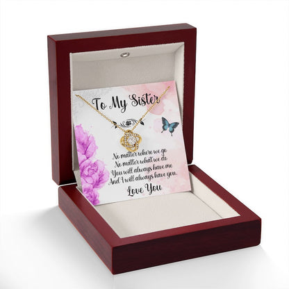 Necklace for sisters: A luxury mahogany-style gift box on a clean white background, featuring a gold love knot necklace alongside a heartfelt sister message card decorated with delicate purple flowers and butterflies.