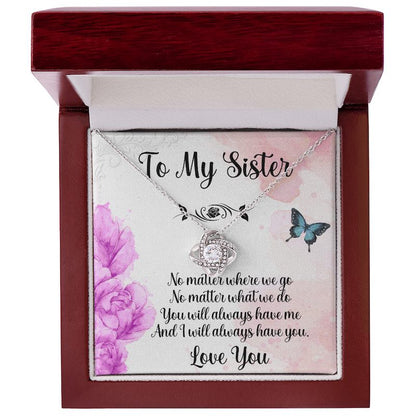 Personalized gift for sister: Silver love knot necklace displayed in an open luxury mahogany-style gift box with a sister message card featuring purple flowers and butterflies.