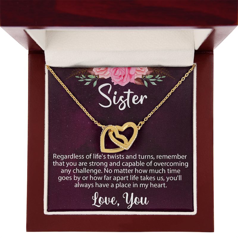 An open luxury mahogany-style wooden gift box displaying a gold interlocking heart necklace on a sentimental "Sister" message card.