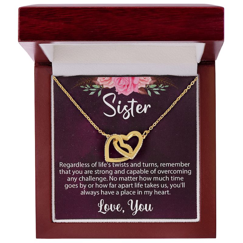 An open luxury mahogany-style wooden gift box displaying a gold interlocking heart necklace on a sentimental "Sister" message card.