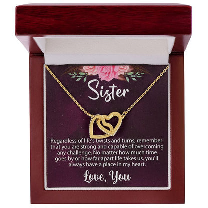 An open luxury mahogany-style wooden gift box displaying a gold interlocking heart necklace on a sentimental "Sister" message card.