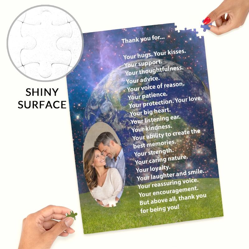 Close-up product display of a custom photo jigsaw puzzle with hands fitting the final corner pieces into place. The puzzle features a couple's oval photo cutout, a romantic thank-you poem, a galaxy space theme, and a circular inset callout text reading "SHINY SURFACE" demonstrating the glossy texture.   