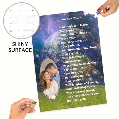 Close-up product display of a custom photo jigsaw puzzle with hands fitting the final corner pieces into place. The puzzle features a couple's oval photo cutout, a romantic thank-you poem, a galaxy space theme, and a circular inset callout text reading "SHINY SURFACE" demonstrating the glossy texture.   