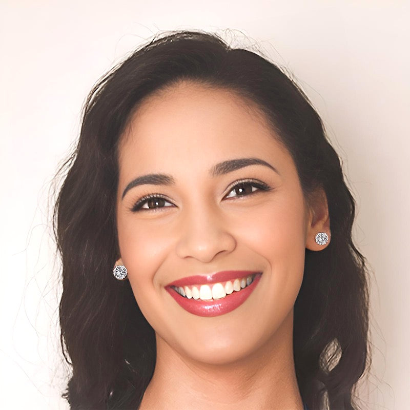 Woman with dark hair and cubic zirconia stud earrings against a plain background