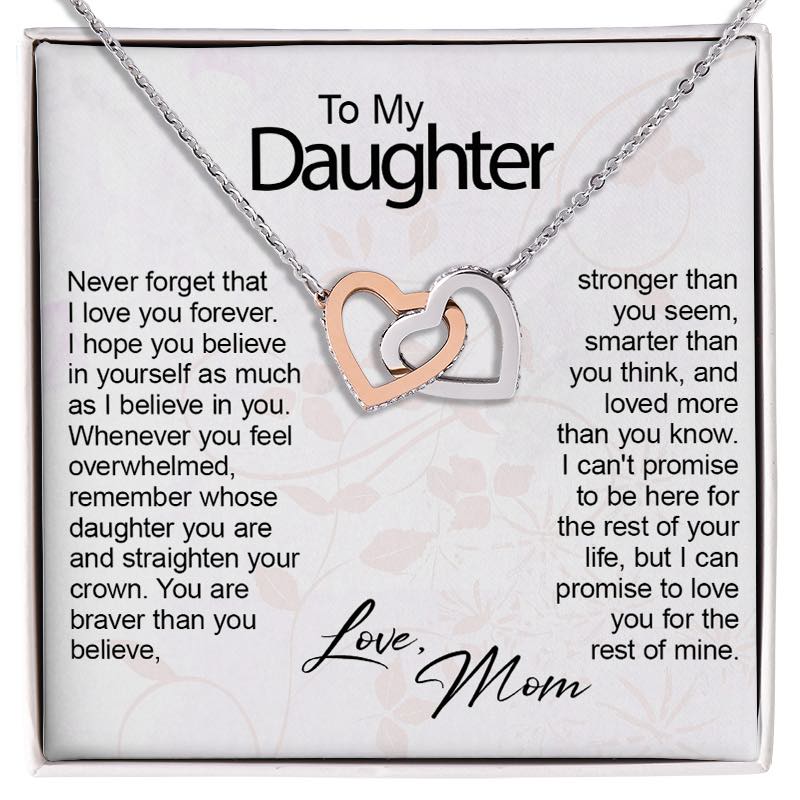 A silver necklace with two interlocking heart charms, one rose gold and one silver, presented on a white gift card with sentimental text addressed to a daughter.