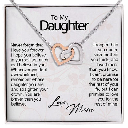 A silver necklace with two interlocking heart charms, one rose gold and one silver, presented on a white gift card with sentimental text addressed to a daughter.