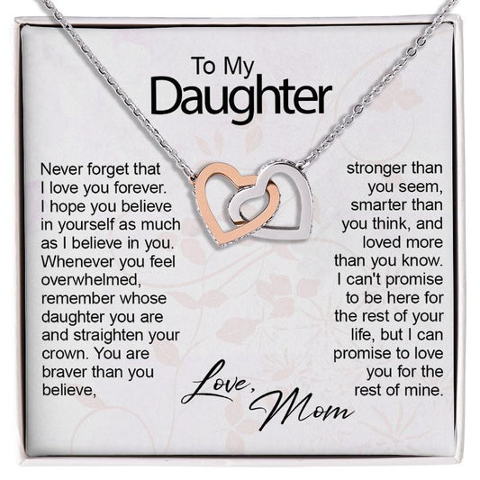 A silver necklace with two interlocking heart charms, one rose gold and one silver, presented on a white gift card with sentimental text addressed to a daughter.