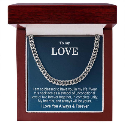 A silver cuban link chain necklace presented inside an open reddish-brown wooden gift box with a blue message card that reads 'To my LOVE' and a sentimental message, presented on a white background.