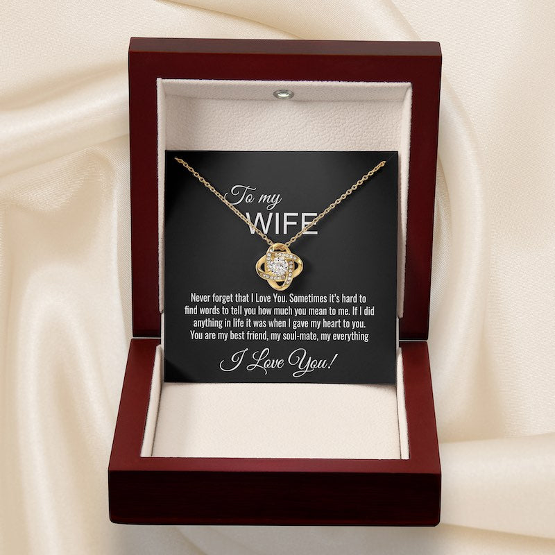Gold knot necklace in a wooden box with a sentimental message card on a beige fabric background