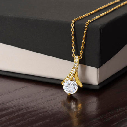Gold ribbon necklace with a zirconia crystal centered pendant on a two tone gift box.