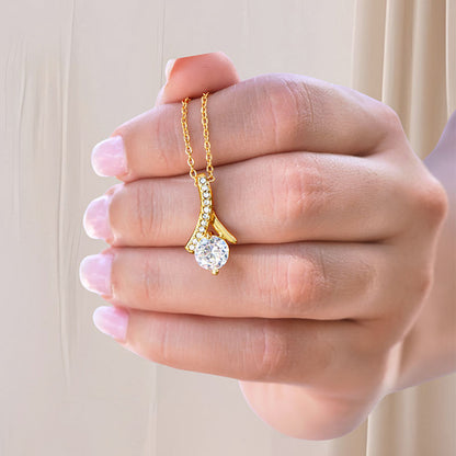 Gold necklace with a ribbon-shaped pendant padded with cubic Zirconia stones and one big round cut Zirconia stone centered, held by a hand against a neutral background