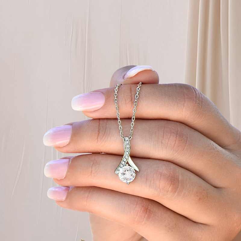 Hand holding a silver ribbon necklace with a round cut Zirconia stone pendant against a neutral background