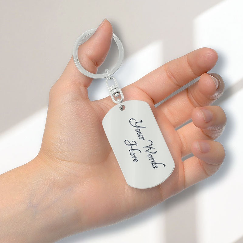 A hand holding a white personalized dog tag keychain with a silver split ring and silver hardware. The dog tag features placeholder script text that reads 'Your Words Here'.